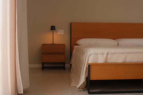 Modern bedroom in Nafura Hotel with wooden bed frame, nightstand, and minimalist furnishings in warm tones