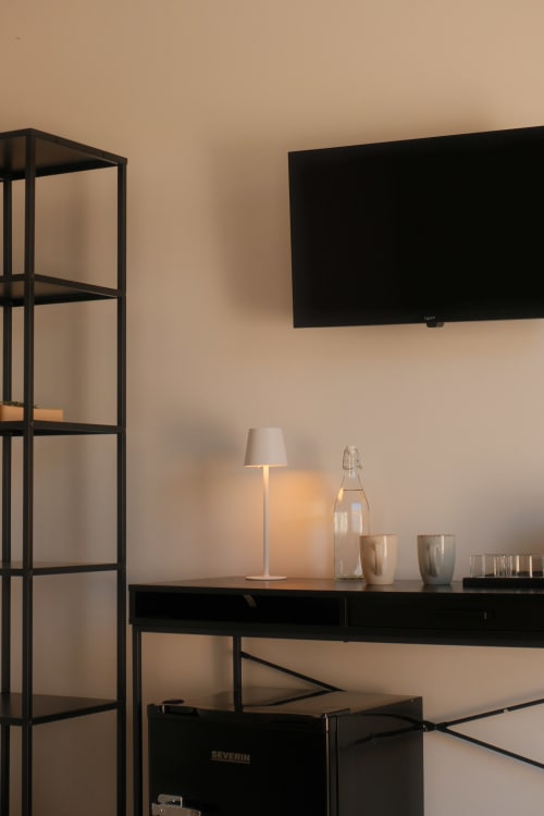 Modern hotel room at Nafura with wall-mounted TV, minimalist desk, lamp, and black metal shelving in Raffadali, Agrigento