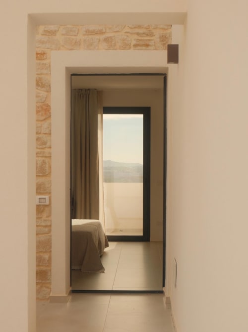 Hallway with stone accent wall leading to Farah room at Nafura hotel in Agrigento, with bedroom and balcony view