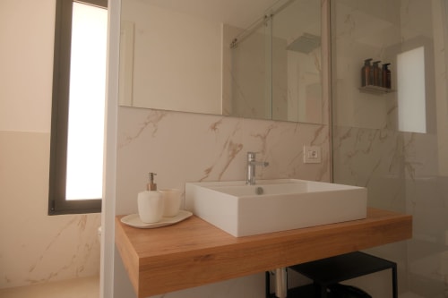Modern bathroom at Nafura hotel in Raffadali with marble walls, vessel sink on wooden vanity, and glass shower enclosure