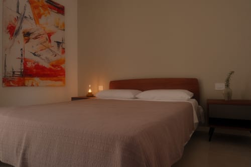 Modern bedroom at Nafura Hotel in Raffadali with queen bed, red headboard, abstract artwork, and ambient lighting