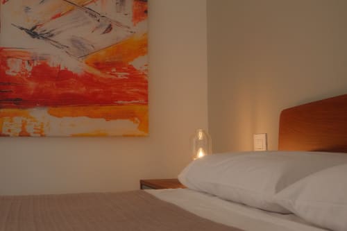 Modern bedroom at Hotel Nafura in Raffadali with white pillows, wooden headboard, abstract red artwork, and ambient lighting