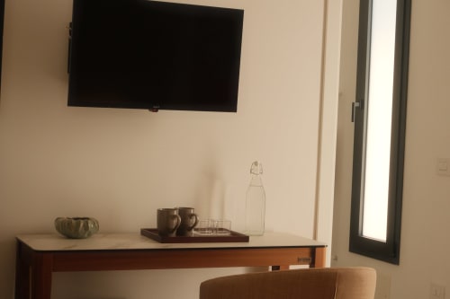 Hotel room desk with wall-mounted TV, water bottle, and glasses at Nafura hotel in Agrigento, Italy