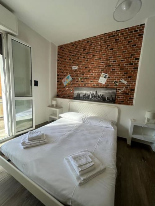 Camera moderna a Gate 10 B&B Bologna con letto bianco, parete in mattoni a vista e arte con skyline cittadino