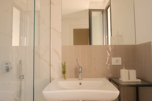 Modern bathroom at Nafura Hotel in Raffadali with white sink, beige tiles, and mirror with garden view access