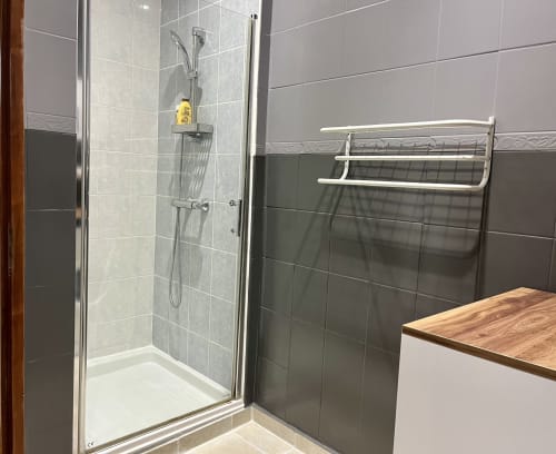 Douche moderne avec pluie de tête et flacon de toilette jaune, étagère chromée, carrelage foncé au Gîte La Vieille Ferme