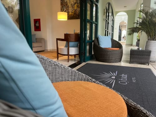 Entrée de l'hôtel Cybade Phu Quoc avec mobilier en rotin, coussins bleus et paillasson dans un hall tropical accueillant