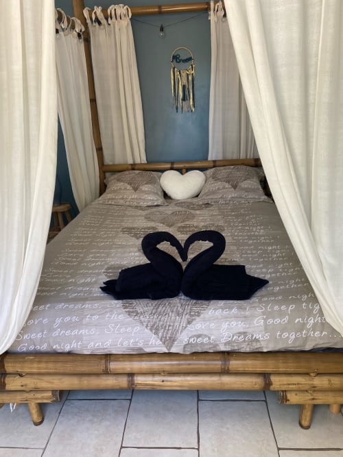 Lit à baldaquin romantique avec voilages blancs, oreillers cygnes noirs formant un cœur, literie thématique aux rêves à Mb Room 4 étoiles