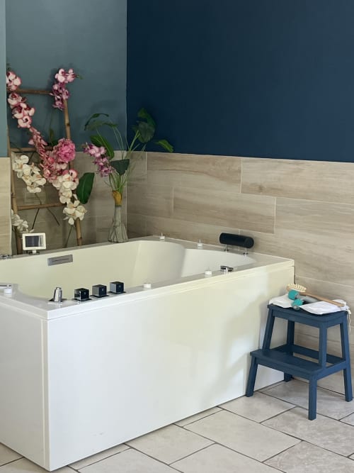 Salle de bains spa luxueuse avec baignoire Jacuzzi blanche, murs en carrelage beige, fleurs roses et marche-pied bleu marine à l'hôtel 4 étoiles Mb Room