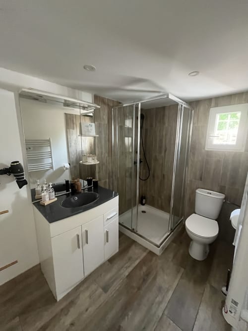 Salle de bain moderne de la Suite Beauté avec douche, lavabo noir, meuble blanc, toilettes et carrelage imitation bois