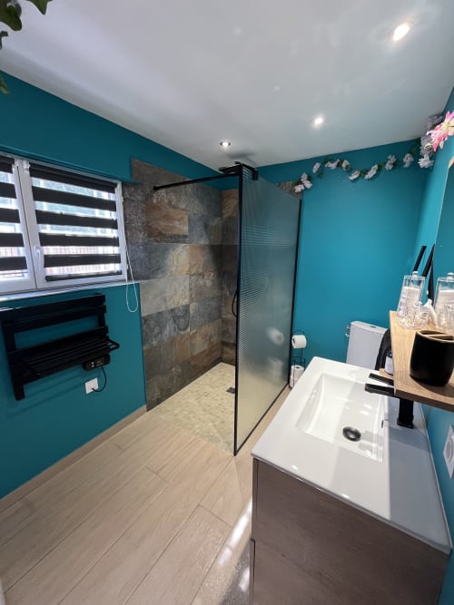 Salle de bain turquoise moderne avec douche à l'italienne, lavabo blanc et revêtement imitation bois à l'hôtel Mb Room 4 étoiles