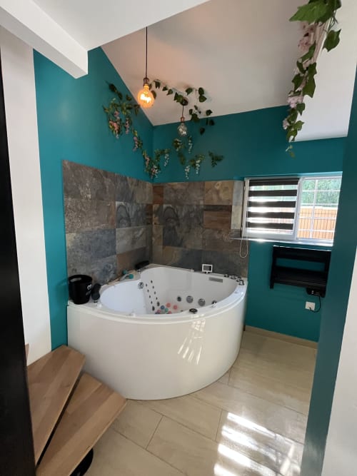 Salle de bain spa luxueuse aux murs bleu canard, jacuzzi blanc d'angle, carrelage ardoise et plantes suspendues à Mb Room 4 étoiles
