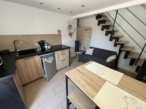 Studio moderne avec kitchenette, canapé noir, table en bois et escalier suspendu à Puget-sur-Argens