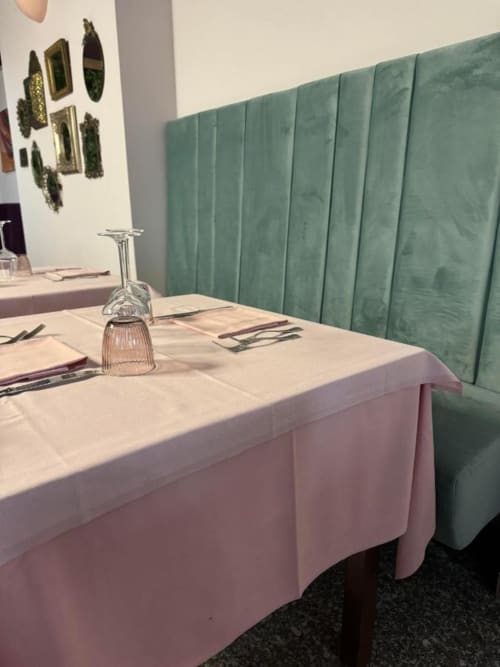 Elegante sala da pranzo con banquette trapuntata verde, tovaglia rosa e apparecchiature presso l'hotel NOI di Vergato, Italia