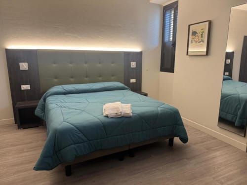 Camera tripla moderna all'hotel NOI di Vergato con coperta teal, testata imbottita, parquet e specchio