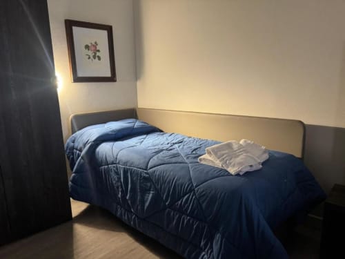 Accogliente camera quadrupla all'hotel NOI DI EVERT di Vergato con biancheria blu, pavimento in legno e quadri floreali incorniciati