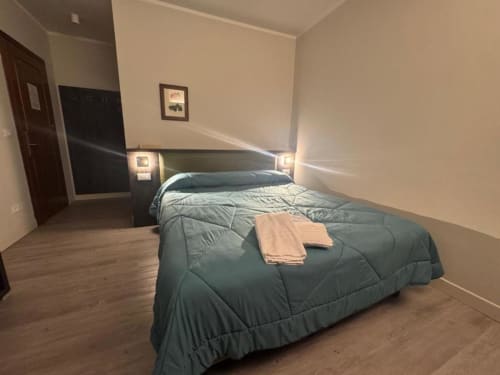 Camera matrimoniale moderna a NOI DI EVERT a Vergato con coperta teal, pavimento in legno, testiera scura con lampade comodino e