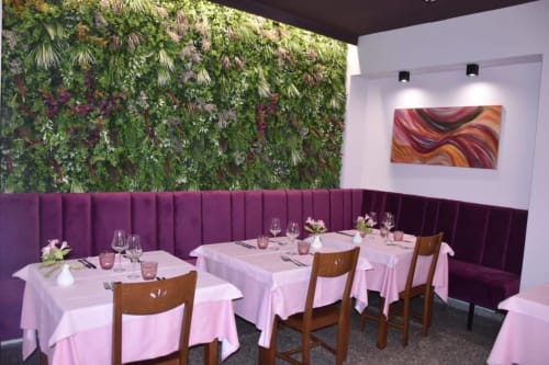 Elegante sala da pranzo con parete verde viva, sedute in banquette viola e tovaglie rosa all'hotel NOI di Vergato