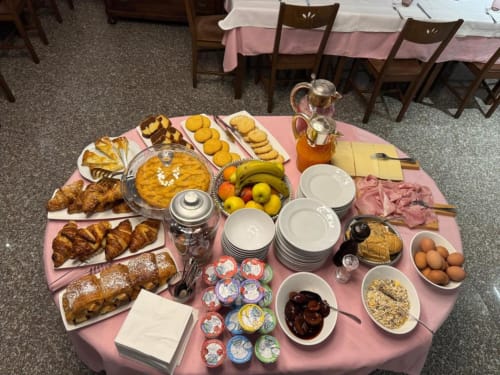 Buffet colazione all'hotel NOI di Vergato con pasticcini, frutta, cereali e bevande su tovaglia rosa