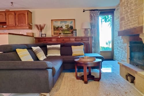 Séjour cosy du Gîte La Vieille Ferme avec canapé gris, mobilier en bois, cheminée et vue sur le jardin à Saint-Geniès