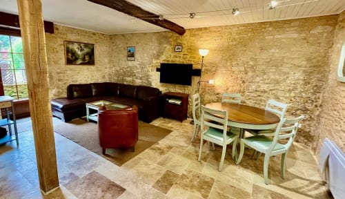 Espace repas et lounge rustique en pierre au Gîte La Vieille Ferme de La Doinie à Saint-Geniès, avec poutres en bois et cuir noir