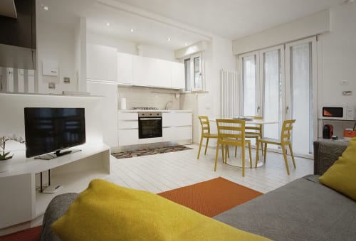 Moderno appartamento open-plan con cucina bianca, sedie gialle, divano grigio, TV e pavimento in ceramica presso La Casetta dei Ronchi