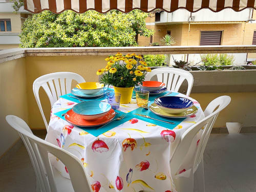 Tavolo colorato sulla terrazza di La Casetta dei Ronchi con tovaglia dipinta, piatti impilati e fiori gialli