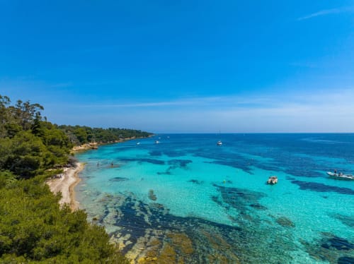 Turquoise Mediterranean cove with sandy beach, pine trees, and boats near Spéracèdes
