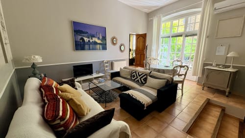 Salon lumineux avec canapé noir, vue sur le jardin par portes-fenêtres, TV et mobilier élégant à Entre vignes