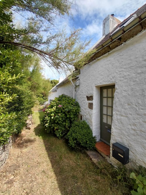 Petite maison en pierre blanche avec porte verte à Sauzon, Belle Île, entourée de jardins luxuriants et d'arbustes fleuris