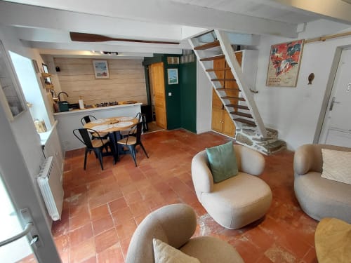 Salon de cottage moderne avec carrelage terre cuite, fauteuils crème, table à manger, cuisine et escalier en bois à Kergue'ch,