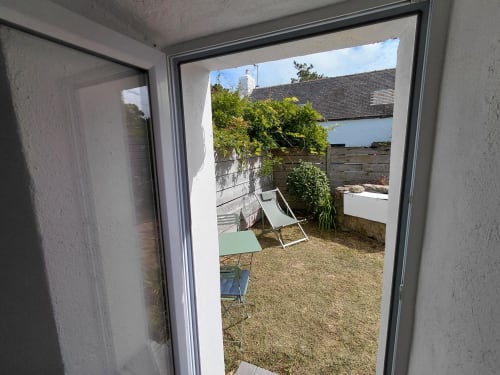 Portes vitrées ouvertes sur un jardin ensoleillé avec transats à la chaumière Kergue'ch, Sauzon, Belle Île en mer
