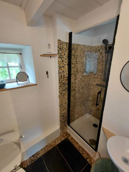 Salle de bain moderne avec douche galets, murs blancs, toilettes, lavabo et fenêtre du gîte Kergue'ch, Belle Île en