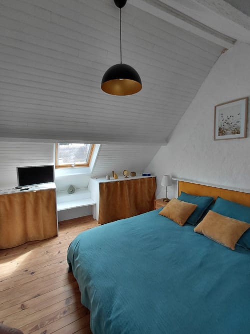 Chambre sous les toits moderne avec literie turquoise, meubles en bois, suspension noire, lucarne et bureau chez Kergue'ch