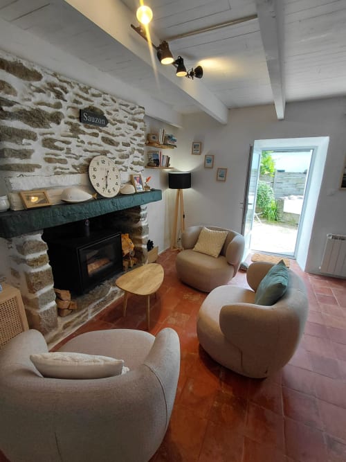 Salon de cottage moderne avec foyer en pierre, fauteuils crème et portes vitrées à Kergue'ch Sauzon, Belle Île