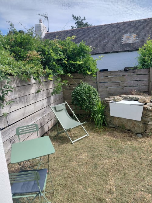 Patio cosy du gîte Kergue'ch à Sauzon avec sièges verts, clôture en bois, plantes en pots et bâtisse en pierre