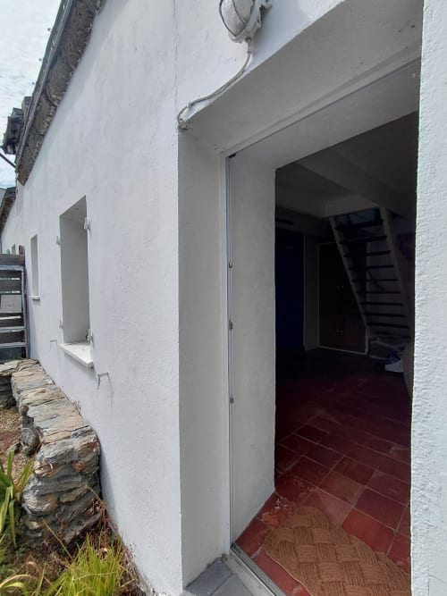 Entrée de chaumière blanche au sol de carrelage rouge et porte ouverte à Kergue'ch Sauzon, Belle Île en Mer