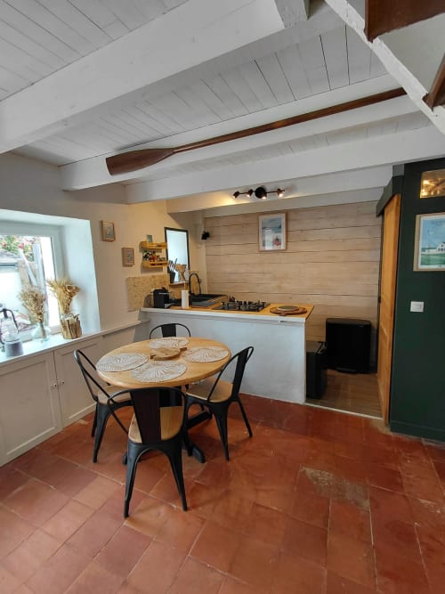 Cuisine ouverte et salle à manger du cottage Kergue'ch à Belle Île en Mer avec table en bois, chaises noires et poutres blanches