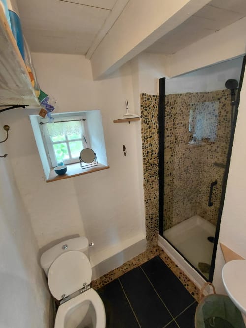 Salle de bains du gîte avec toilettes, douche ouverte aux galets, fenêtre et miroir à Loc'Maria Belle Île en Mer