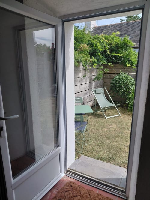 Porte vitrée ouverte sur la terrasse jardin avec transats et végétation luxuriante du gîte Loc'Maria, Belle Île en Mer