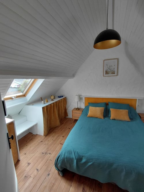 Chambre mansardée moderne avec lit bleu-vert, parquet, lucarne et suspension noire dans un gîte de Belle Île en Mer