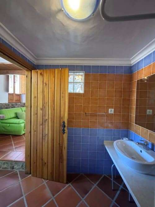 Banheiro da pousada T Monte em Porto Côvo com azulejos de terracota, paredes azuis, pia branca e porta de madeira para o quarto