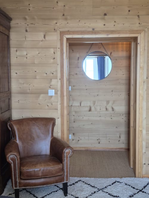 La chambre L'Atlantique à La Maison De Fleurat avec fauteuil en cuir, lambris en pin noué et miroir rond au-dessus de la porte en bois.
