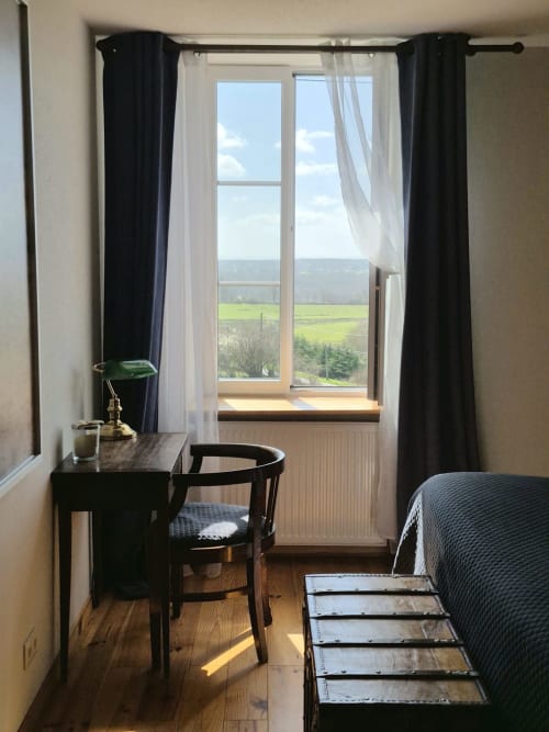 Chambre L'Atlantique à La Maison De Fleurat avec vue sur le jardin par portes-fenêtres, rideaux noirs, bureau et lit
