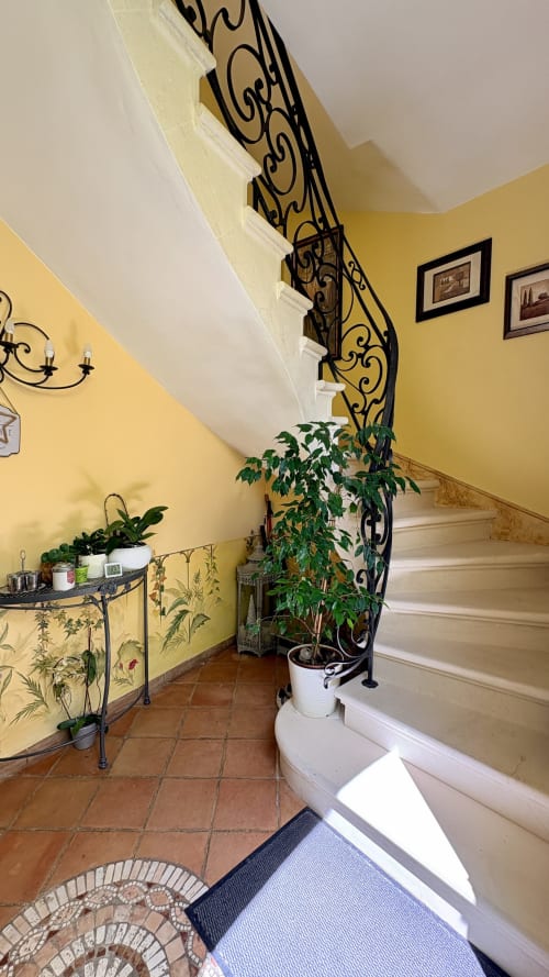 Élégant escalier à rampe en fer forgé dans l'entrée aux murs jaunes de l'hôtel Entre vignes et dentelles, Courthézon