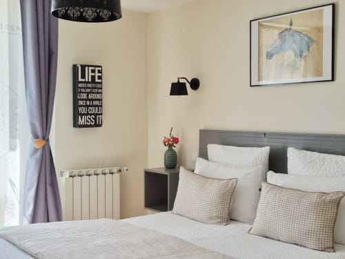 Chambre confortable à La Maison De Fleurat avec tête de lit grise, oreillers blancs, coussins à carreaux et décoration murale inspirante