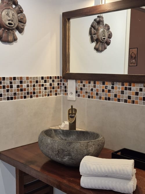 Luxueux lavabo de La Maison De Fleurat avec vasque en pierre, carrelage décoratif et masques africains