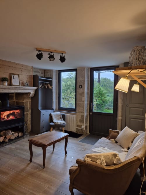 Salon chaleureux avec cheminée, vue sur le jardin, mobilier en bois et luminaires au plafond à La Maison De Fleurat