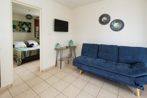 Cottage Kaz La Brise à Otantik Caribbean au Gosier avec canapé bleu, télévision et vue sur la chambre par l'encadrement de la porte
