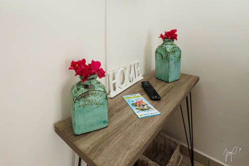 Table de nuit en bois dans le cottage Kaz La Brise avec vases verts vintage, fleurs rouges et décoration HOME à Otantik Caribbean